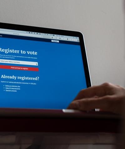 A close up of a laptop screen with a voter registration website and a person's hand on the keyboard.